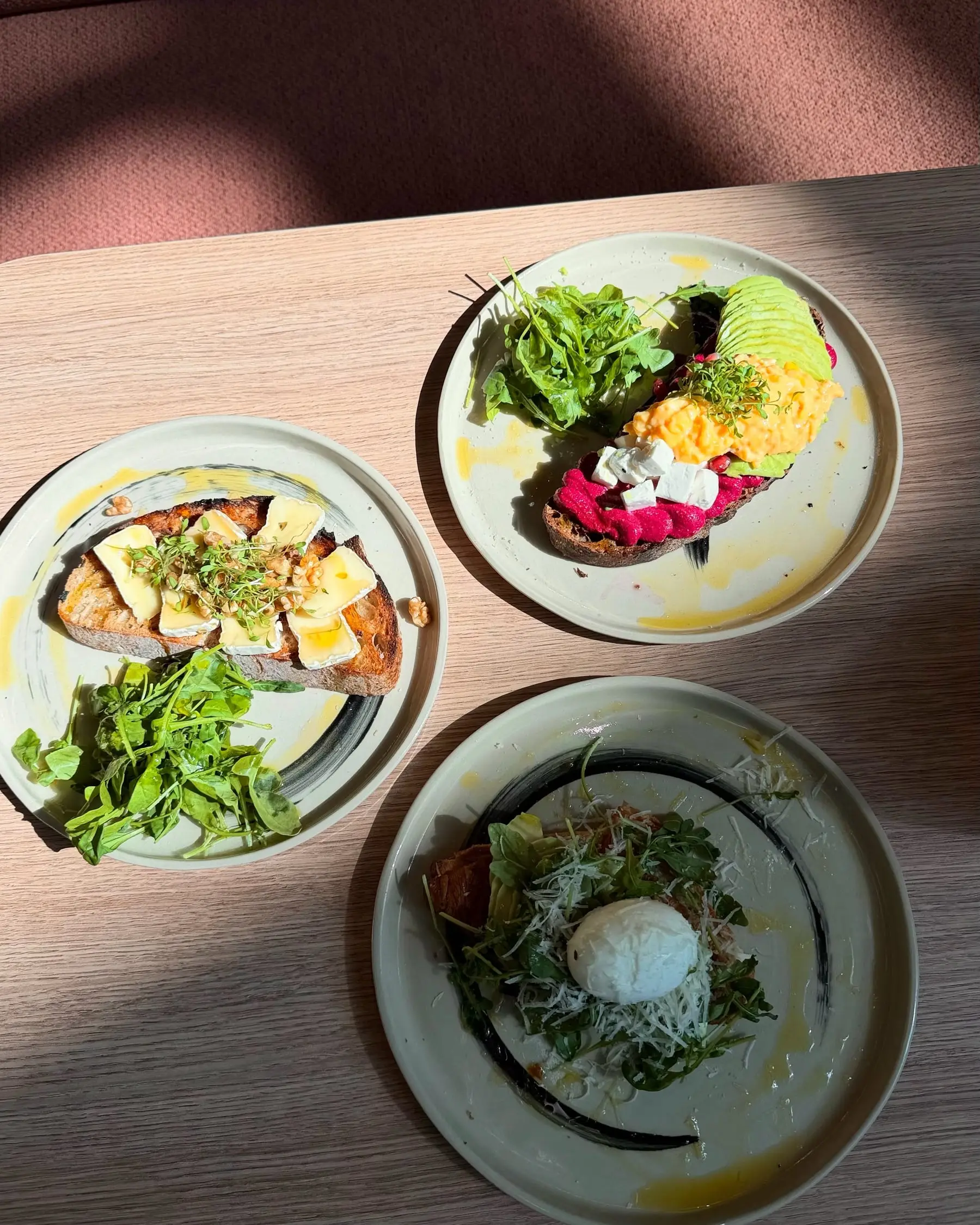 Drei Frühstücksteller von oben: belegte Sauerteigbrote und ein pochiertes Ei auf Salat