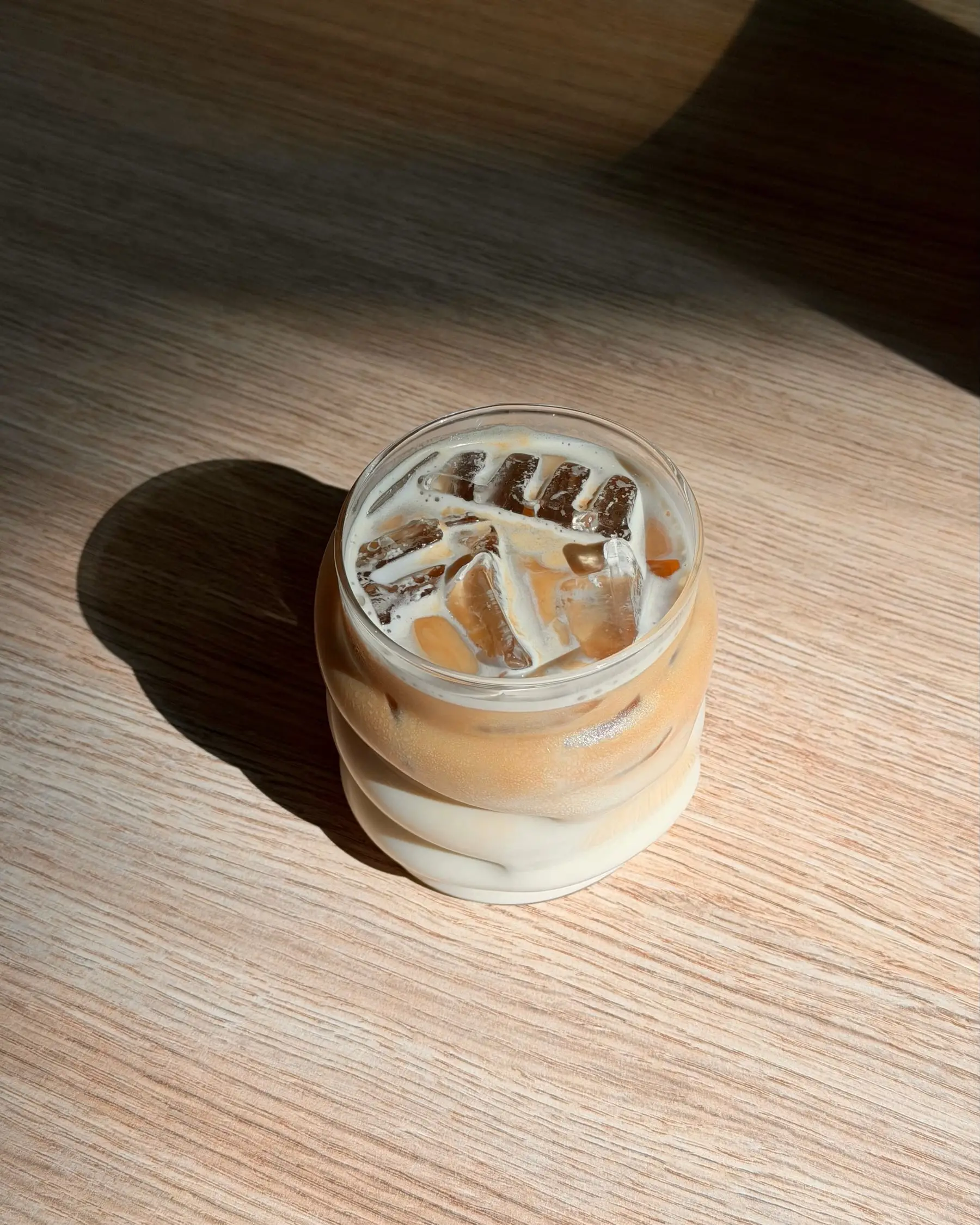 Iced Latte im gewellten Glas auf einem sonnigen Holztisch