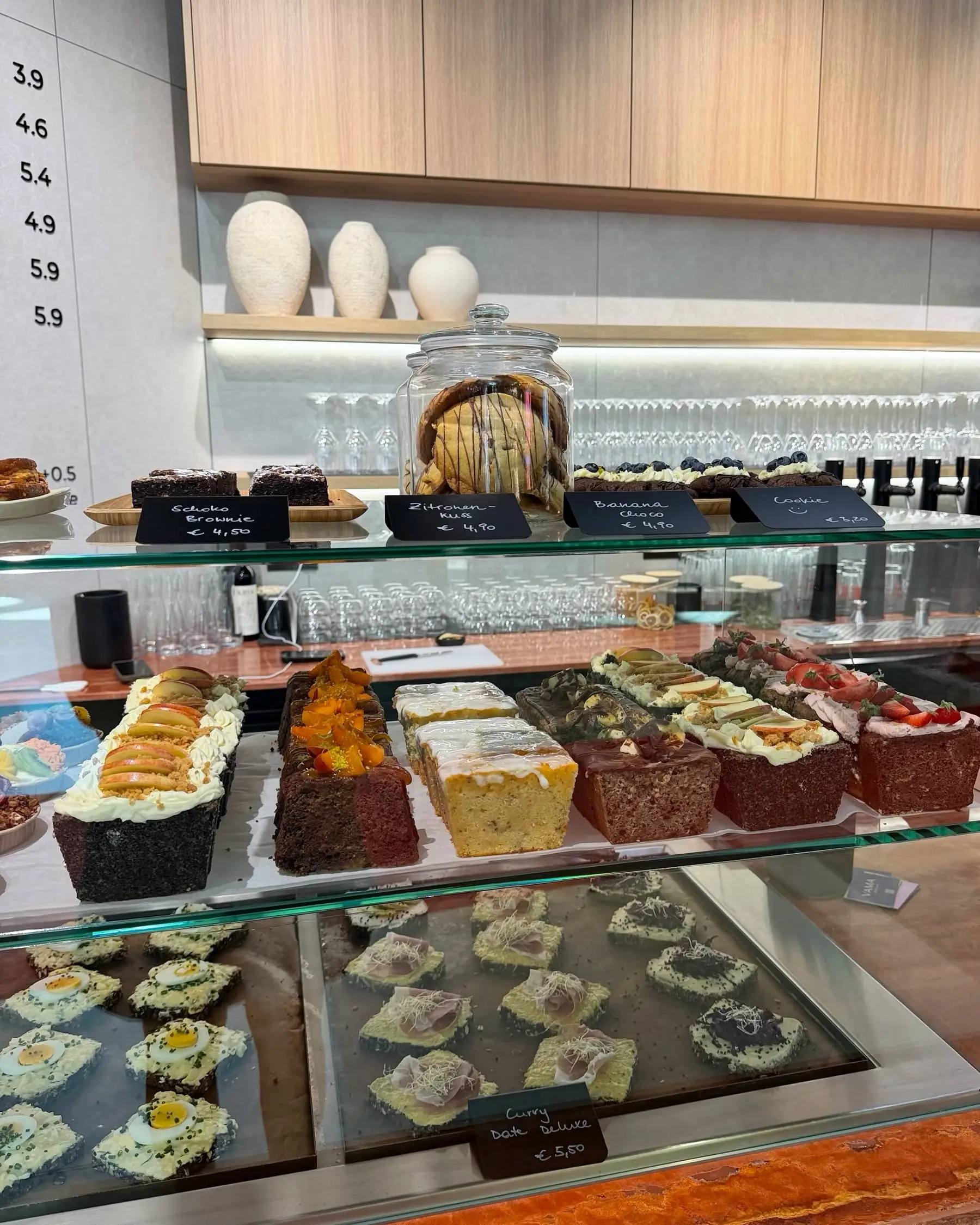 Lange Glasvitrine mit Blechkuchen und Loaf Cakes, dahinter helle Holzregale mit Gläsern