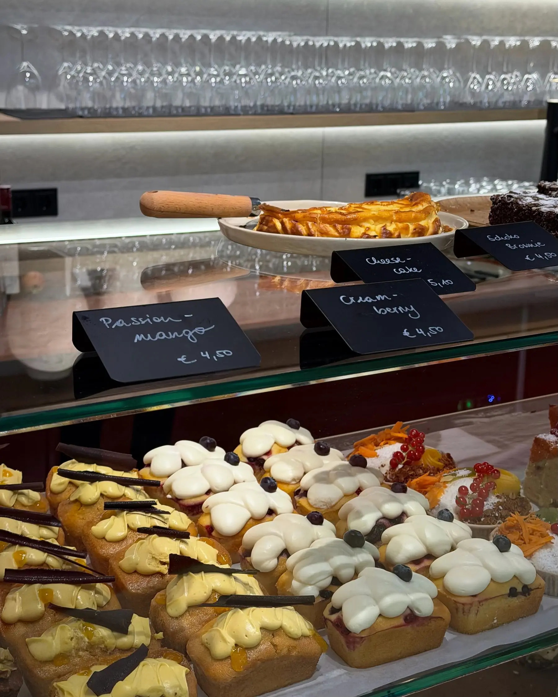 Glasvitrine mit Loaf Cakes und Frosting, dahinter Kuchen mit handgeschriebenen Preisschildern